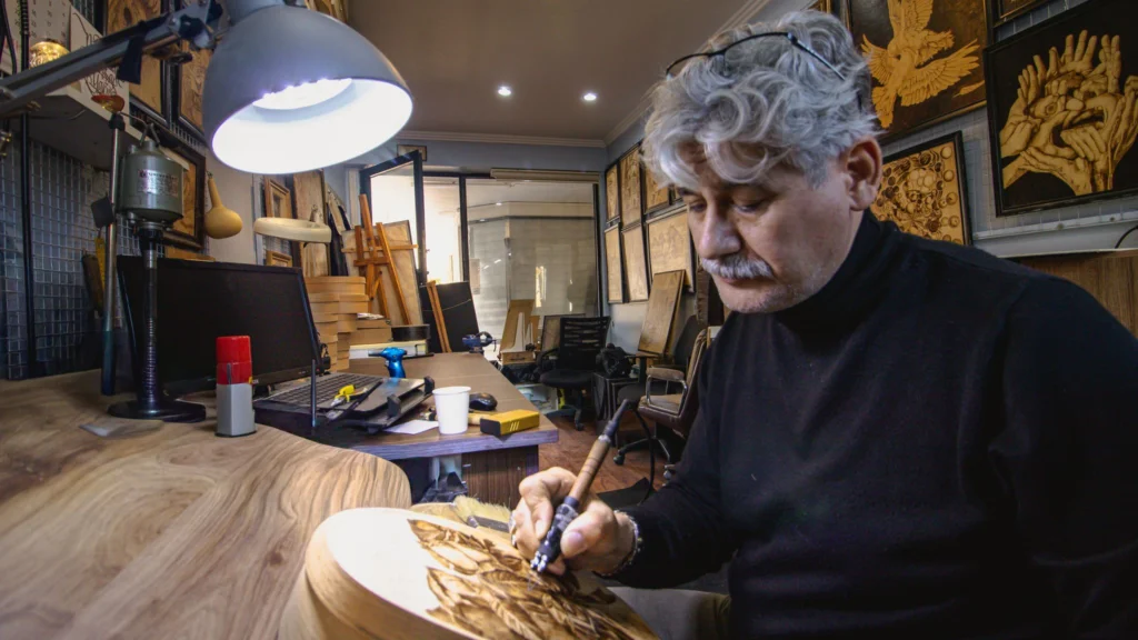 Sculptură manuală cu dalta alături de o mașină CNC în atelier
